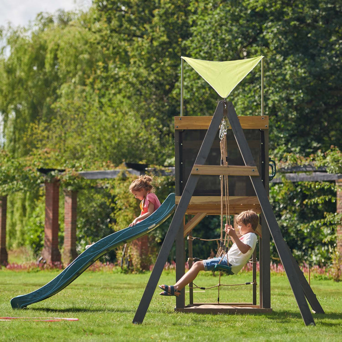 Side view of Plum Play's Siamang Wooden Playcentre Climbing Frame in a lawn with children sliding and swinging