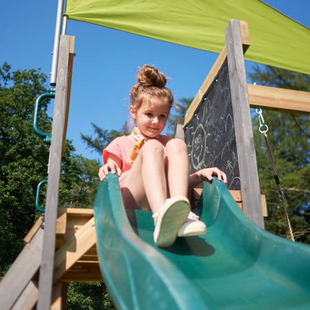 Smiling girl about to slide in the 8 feet green wave slide of Plum Play's Siamang Wooden Playcentre