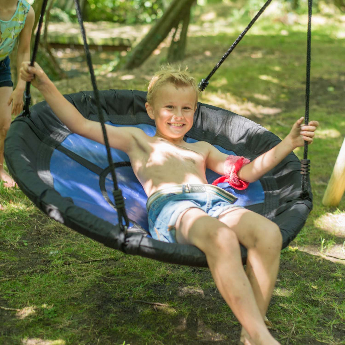 Boy smiling while lounging in the nest seat of Plum Play's Spider Monkey Wooden Nest Swing Set