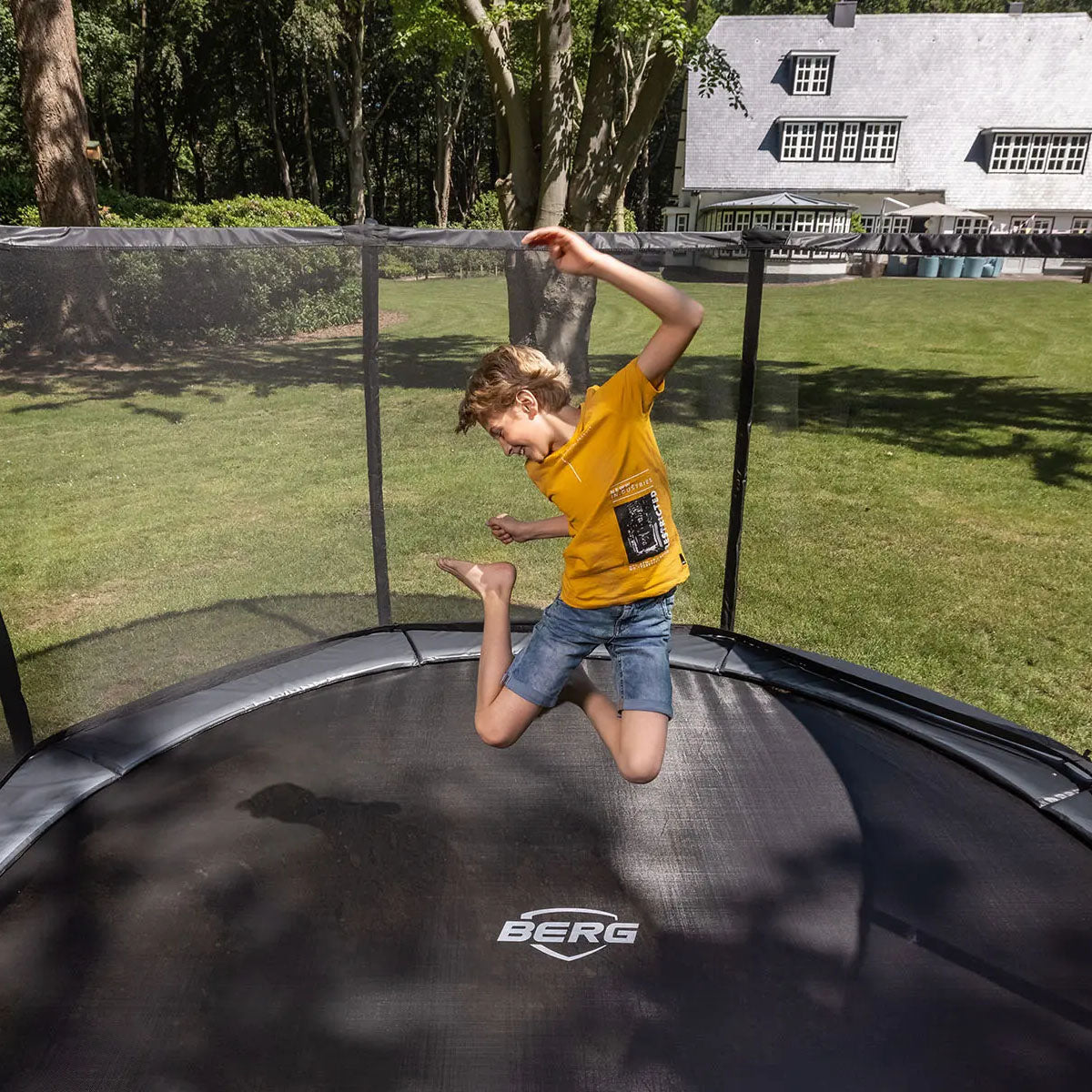 a boy jumping happily inside the BERG Elite InGround Round Trampoline with Safety Net Deluxe