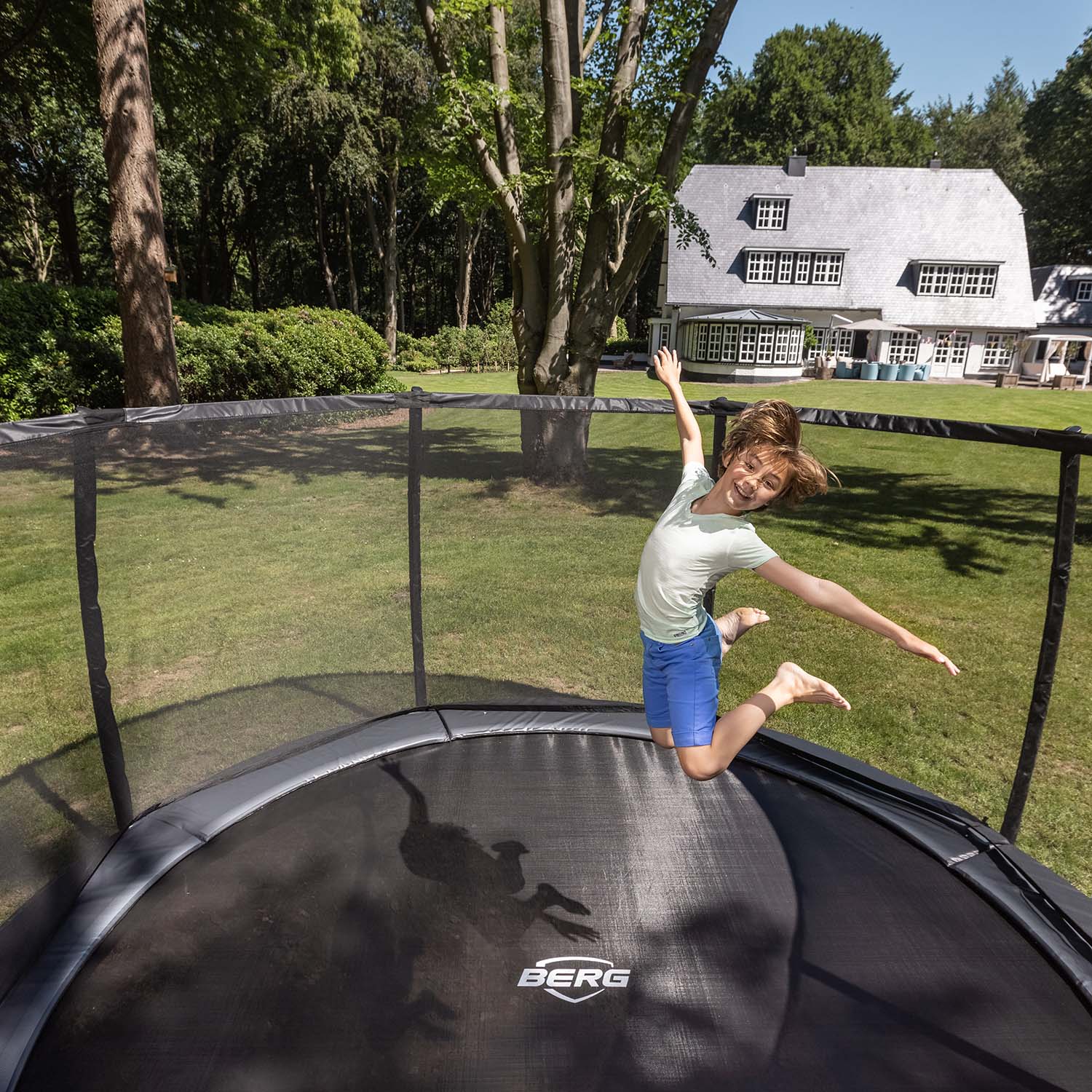 smiling child playing inside the BERG Elite InGround Round Trampoline with Safety Net Deluxe