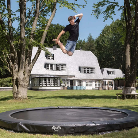 a teenage boy happily jumping on a ERG SPORTS Champion InGround Round Trampoline