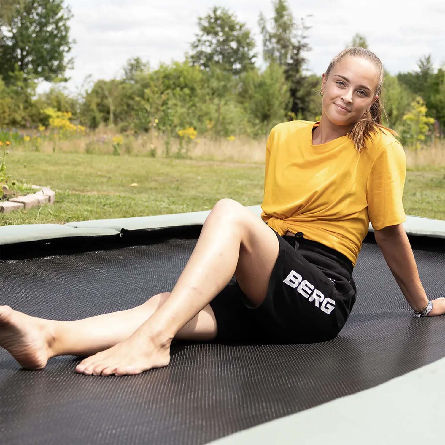 a young athlete sitting on a BERG SPORTS Ultim Champion ECO FlatGround Rectangular Trampoline