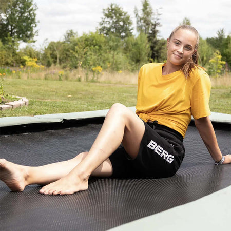 a young athlete sitting on a BERG SPORTS Ultim Champion ECO FlatGround Rectangular Trampoline