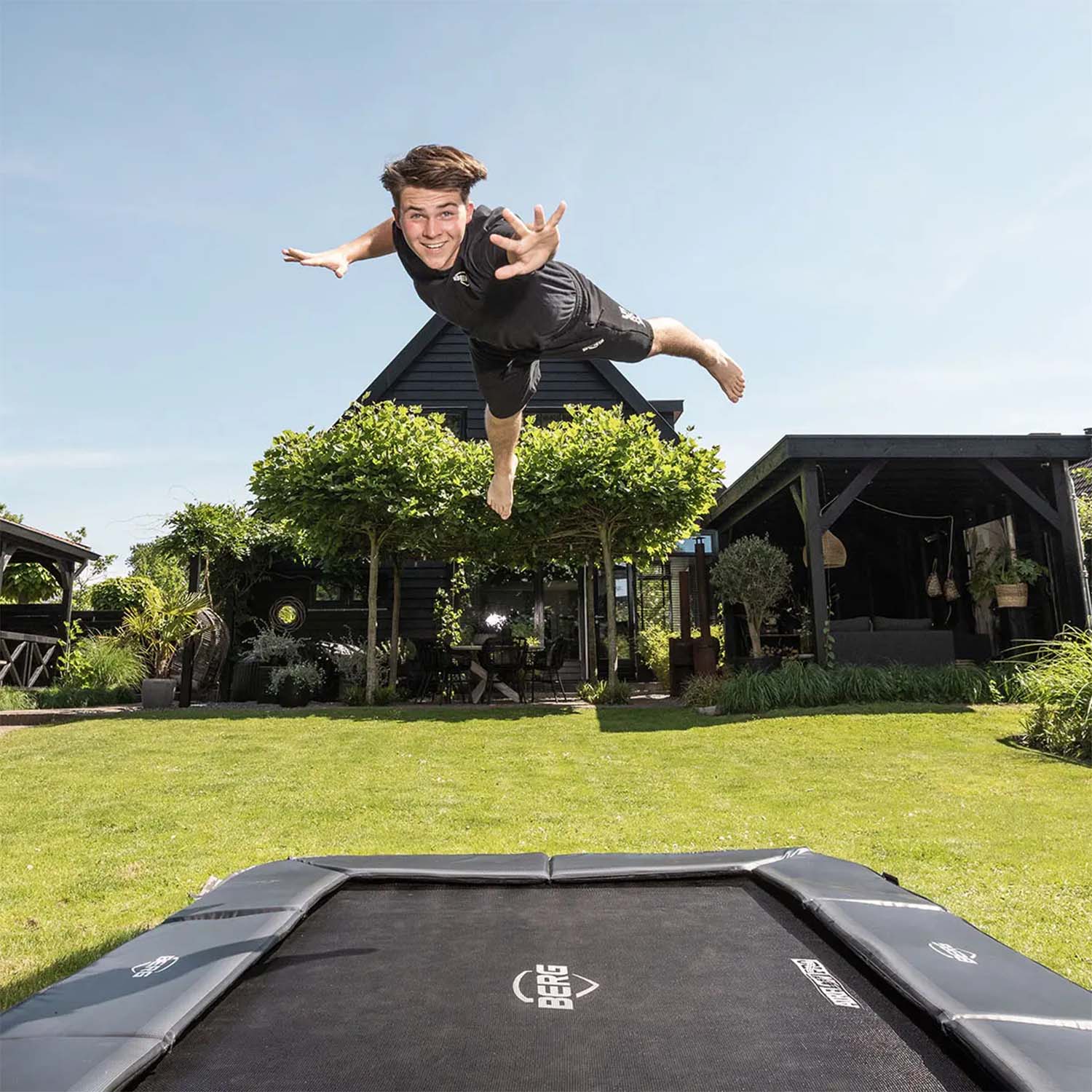 a trained athlete happily jumping on a BERG SPORTS Ultim Champion FlatGround Rectangular Trampoline