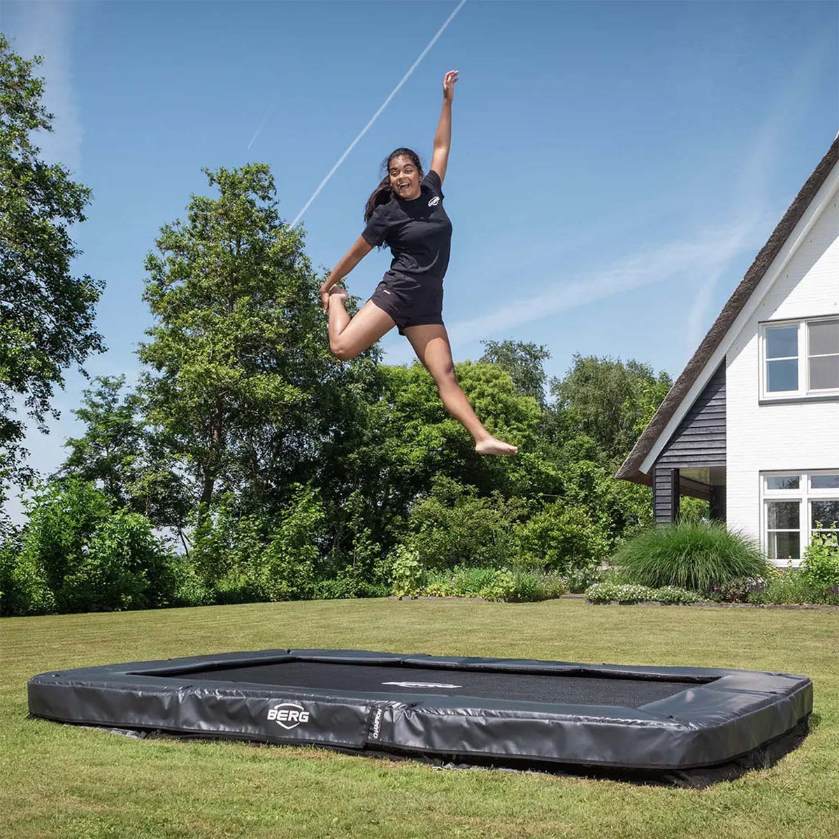 teenage girl happily playing on BERG SPORTS Ultim Champion InGround Rectangular Trampoline