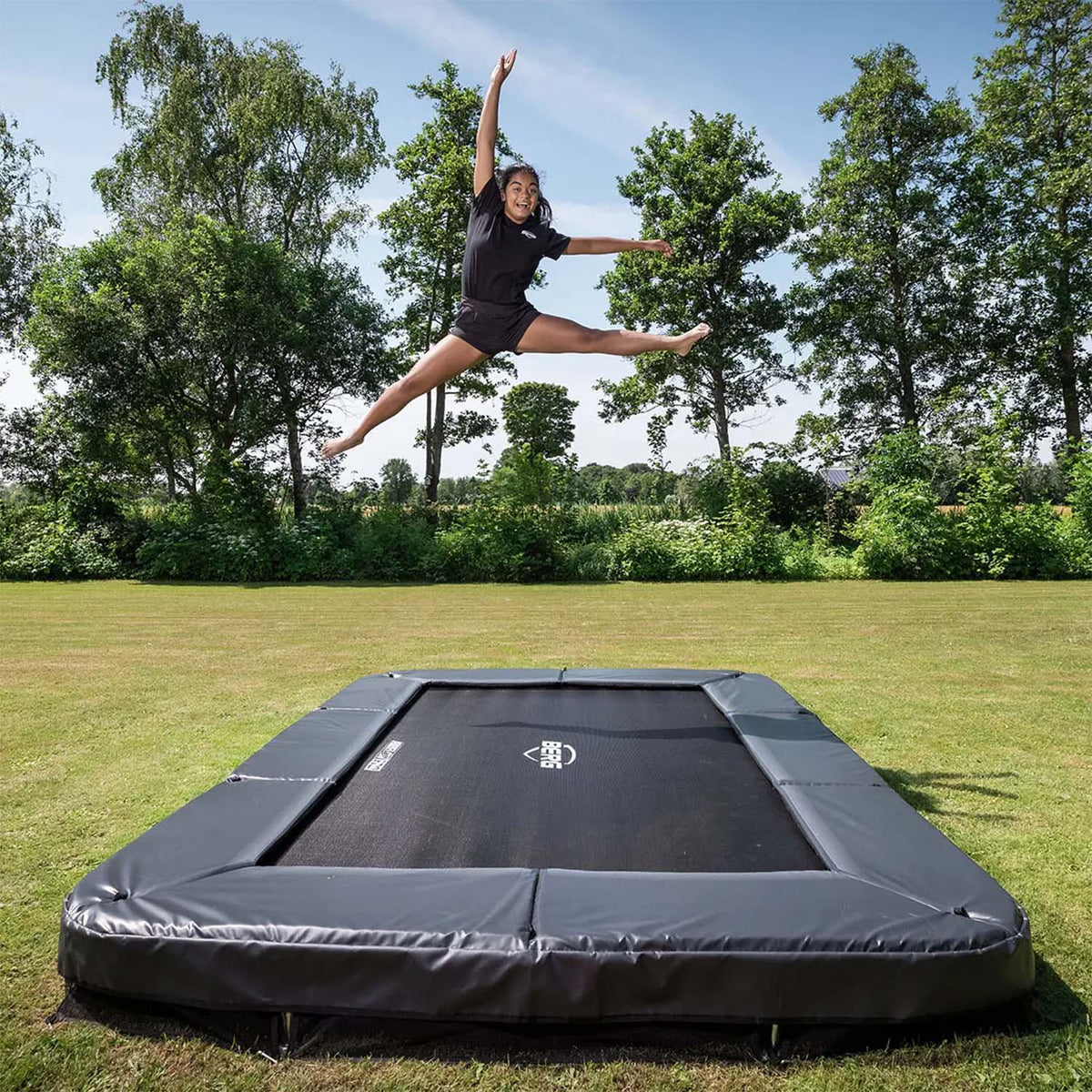 a teenage girl jumping on a BERG SPORTS Ultim Champion InGround Rectangular Trampoline