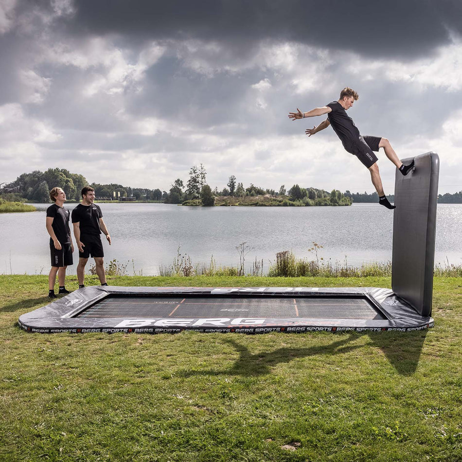 athletes training advanced routines on a BERG SPORTS Ultim Pro Bouncer FlatGround Rectangular Trampoline with AeroWall