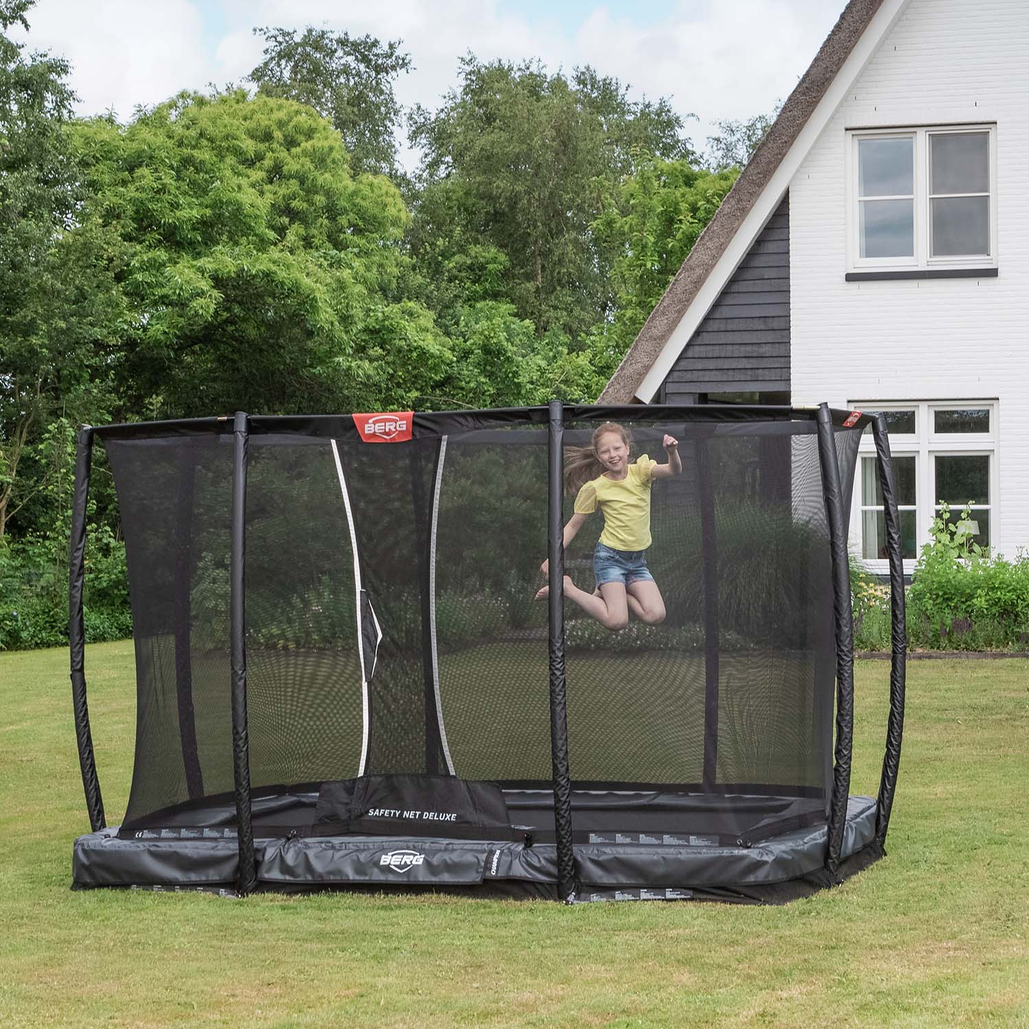 girl playing in the BERG Ultim Champion InGround Rectangular Trampoline with Safety Net Deluxe in Grey colour