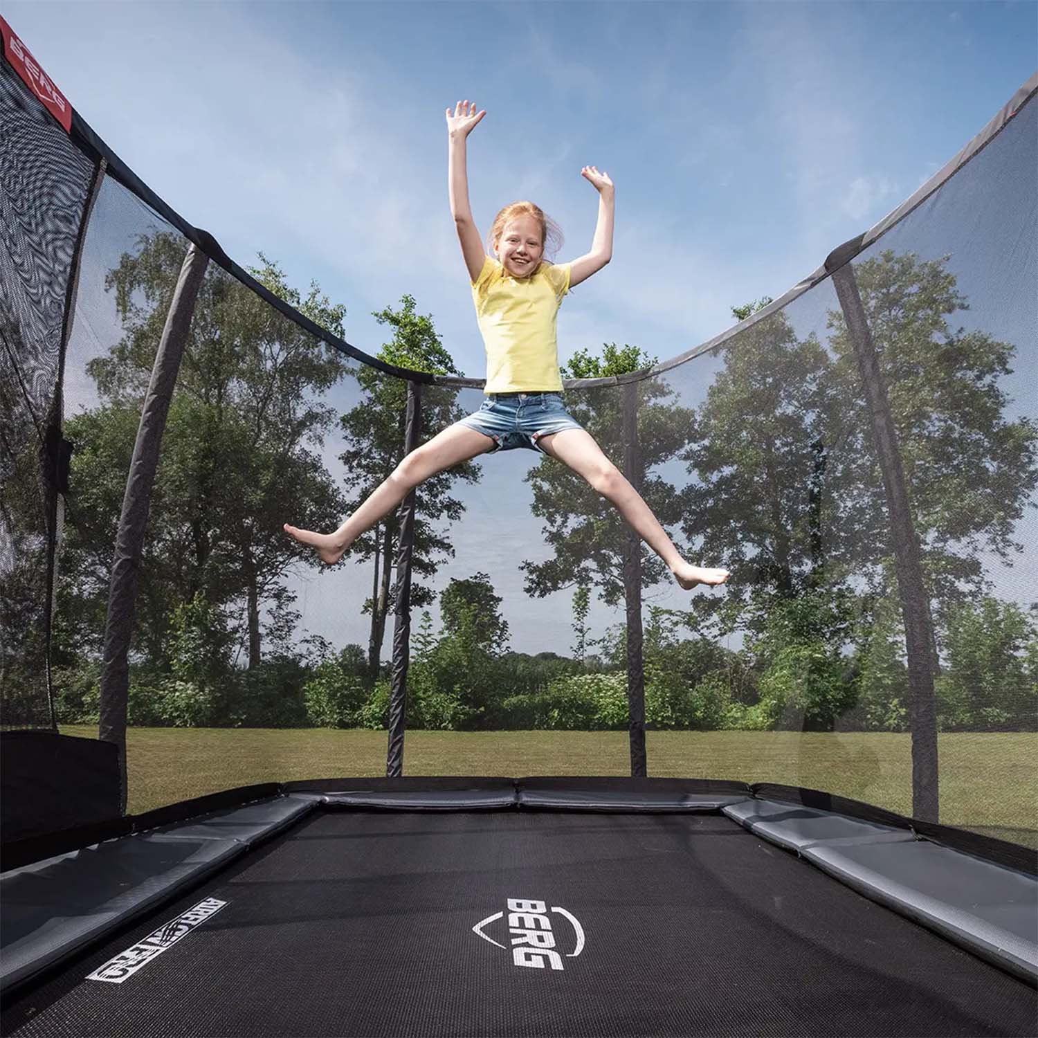 girl jumping happily inside BERG Ultim Champion InGround Rectangular Trampoline with Safety Net Deluxe in Grey colour